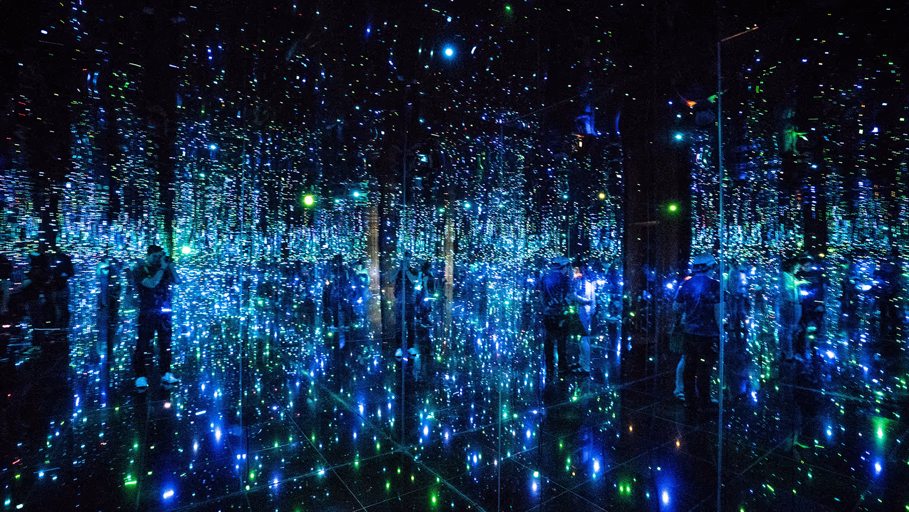 Room filled with blue and green LED lights creating an infinity mirror effect with reflections of people.